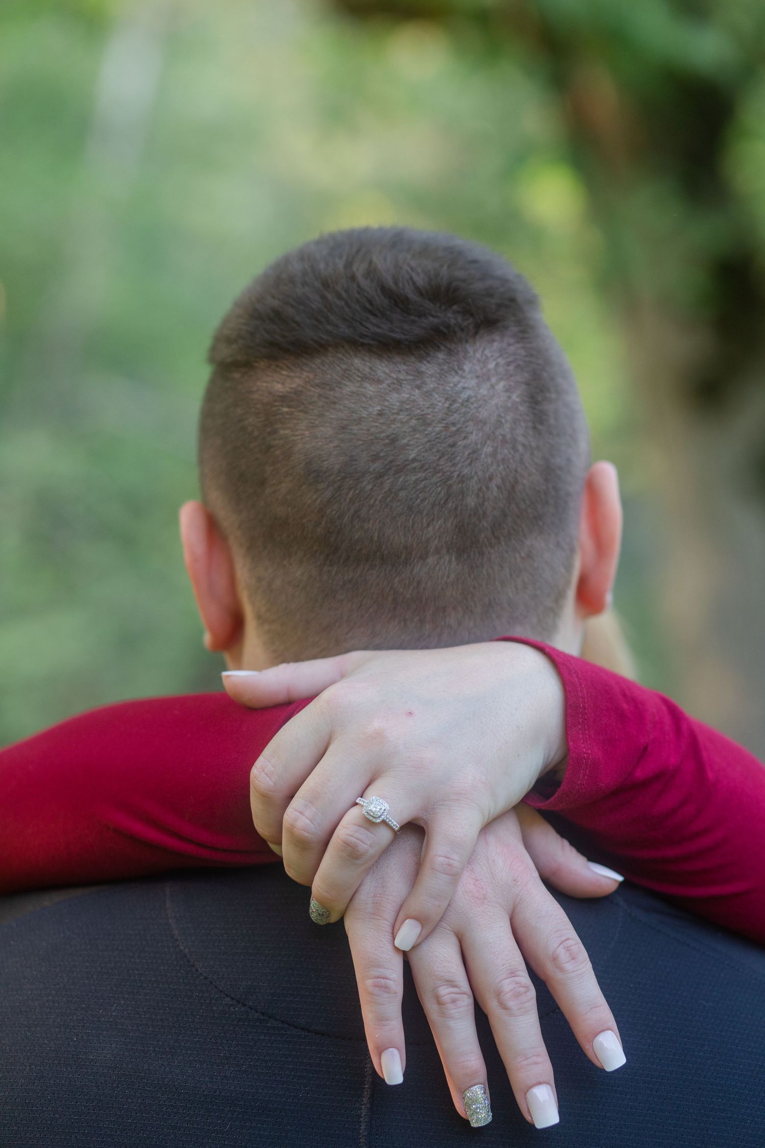 Close-up detail of hands with an engagement ring resting on a black shirt.
