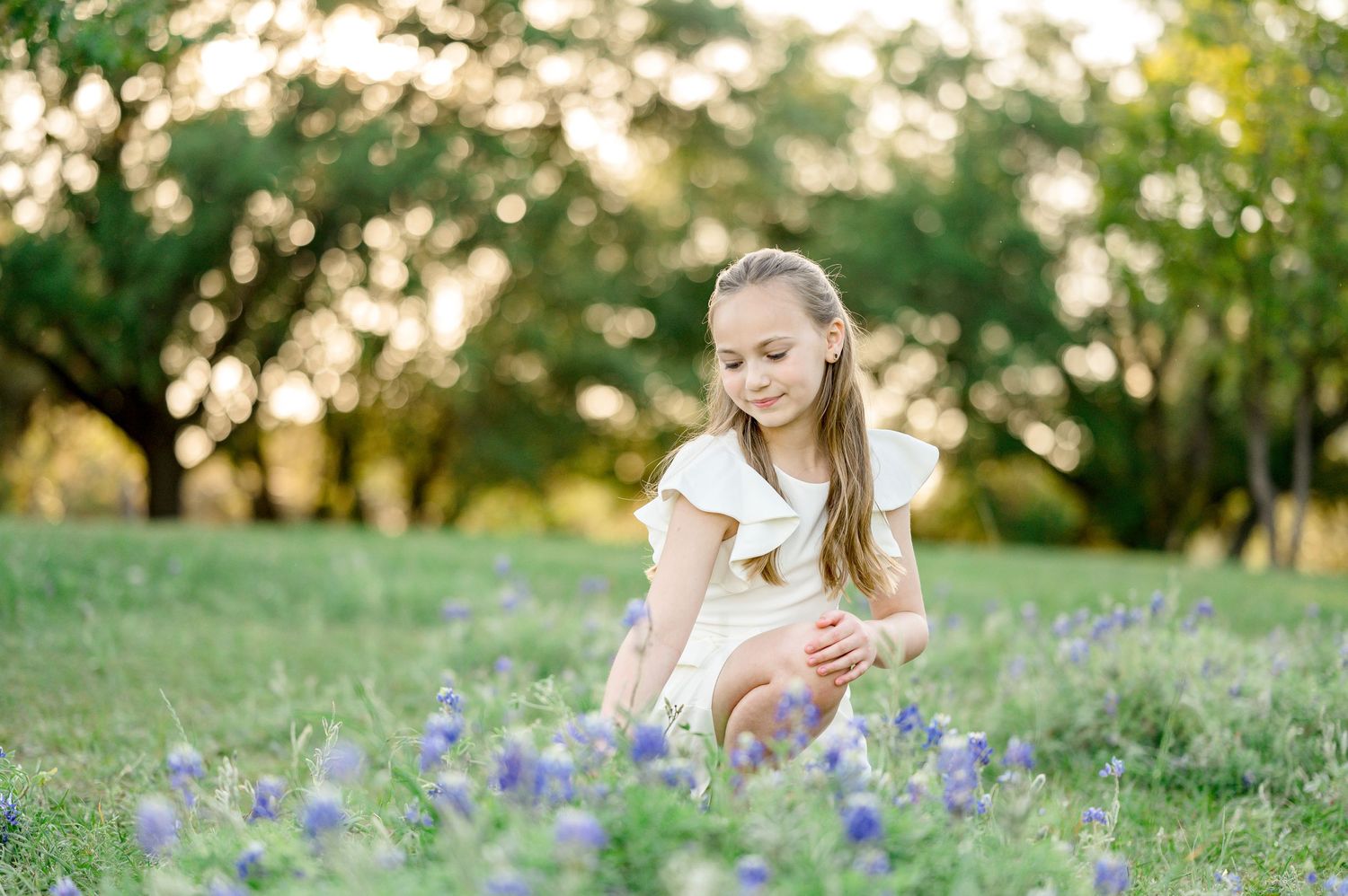 Children sitting in sunny meadow with purple wildflowers during golden hour.