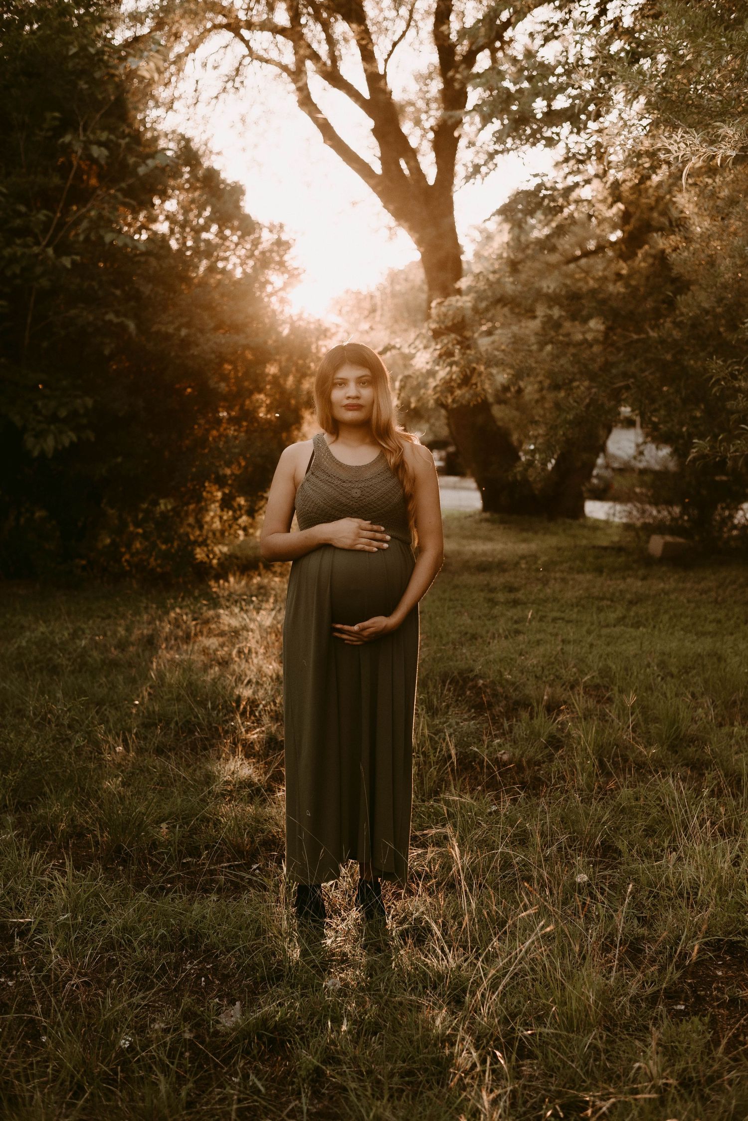 Serene maternity photo with sunset glow through trees.