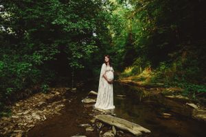 A couple shares an intimate moment by a wooden bridge in a serene forest setting.