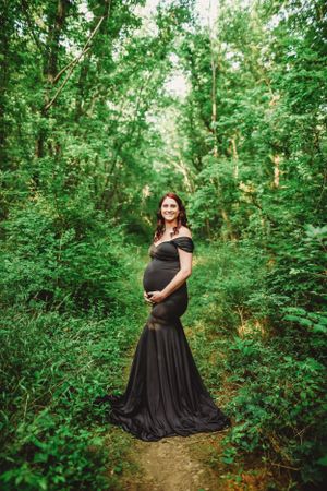 Elegant maternity photos featuring woman in black dress among lush greenery.