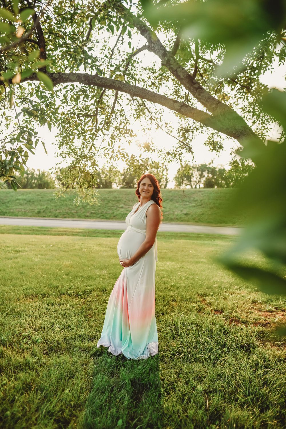 A colorful tie-dye dress flows in the breeze as someone poses in a grassy field at sunset.