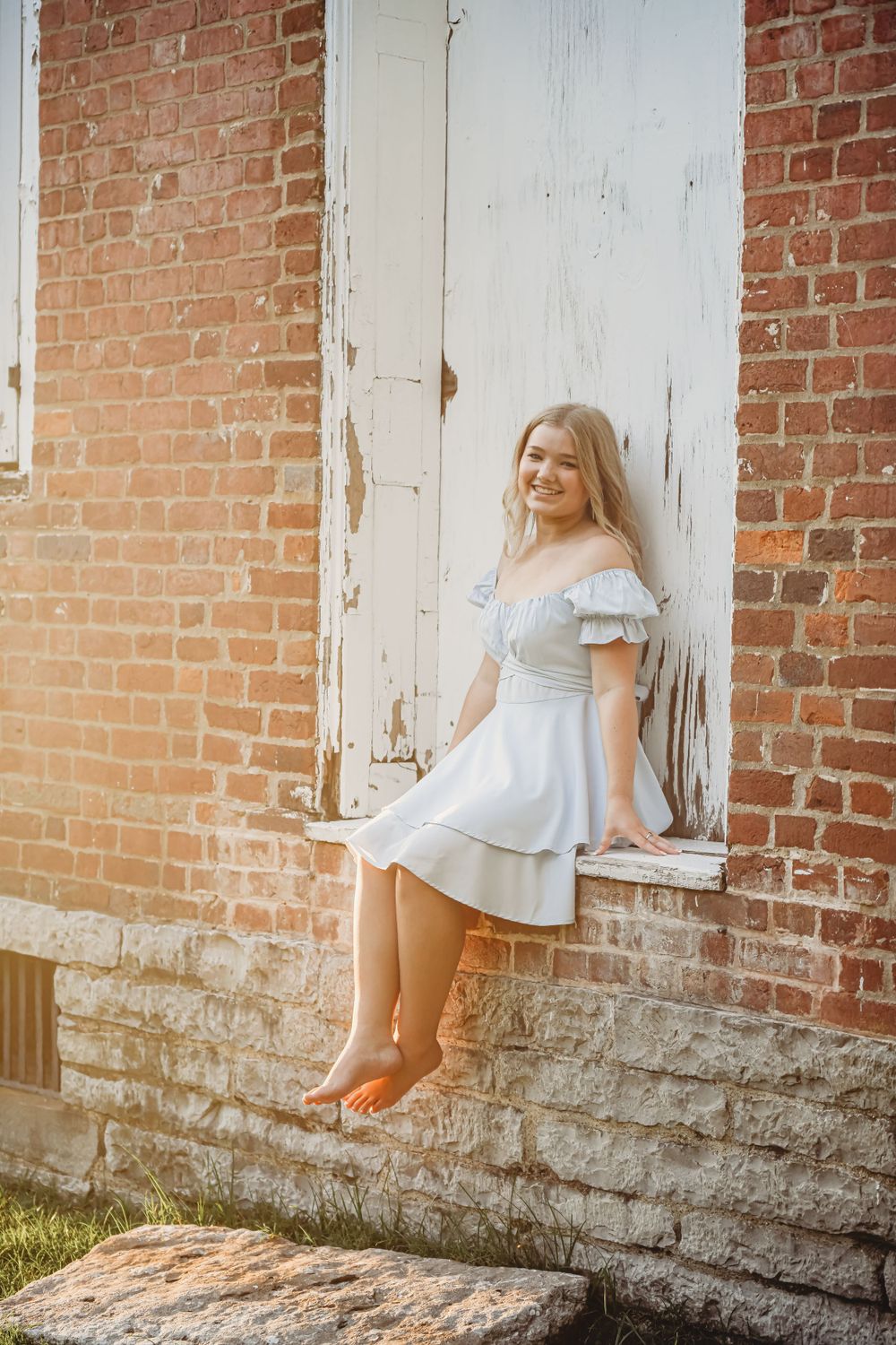 Light blue dress twirls against weathered brick wall and white door in vintage setting.