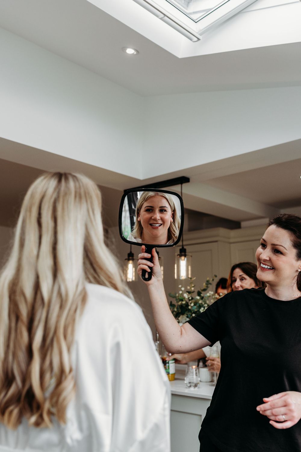 Two people sharing a joyful moment while looking in a handheld mirror during wedding preparations.