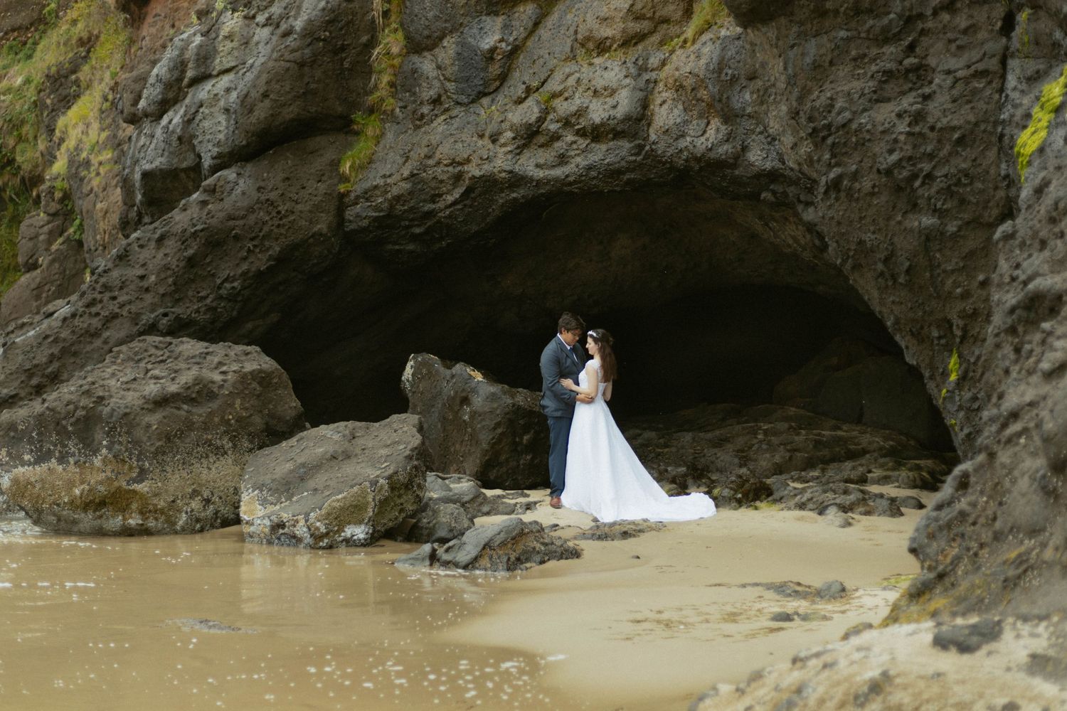 A romantic wedding photo session in a scenic beach cave with rocky cliffs and sand.