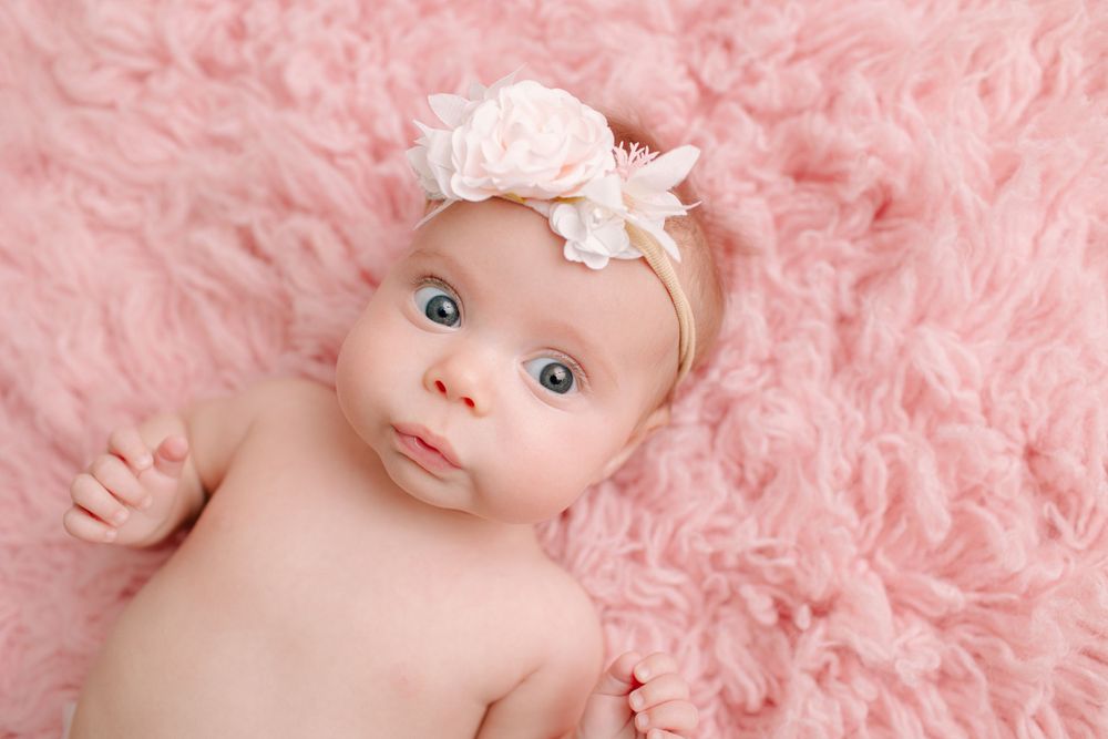 Baby lying on soft pink fur blanket wearing delicate floral headband during professional studio photoshoot.