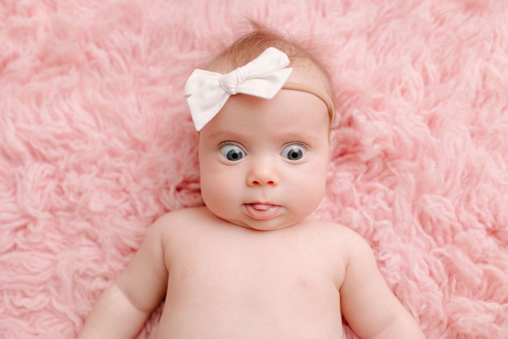 Baby portrait on pink furry backdrop with white bow headband accessory.