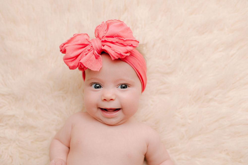 Baby wearing coral bow headband smiling during professional photography session.