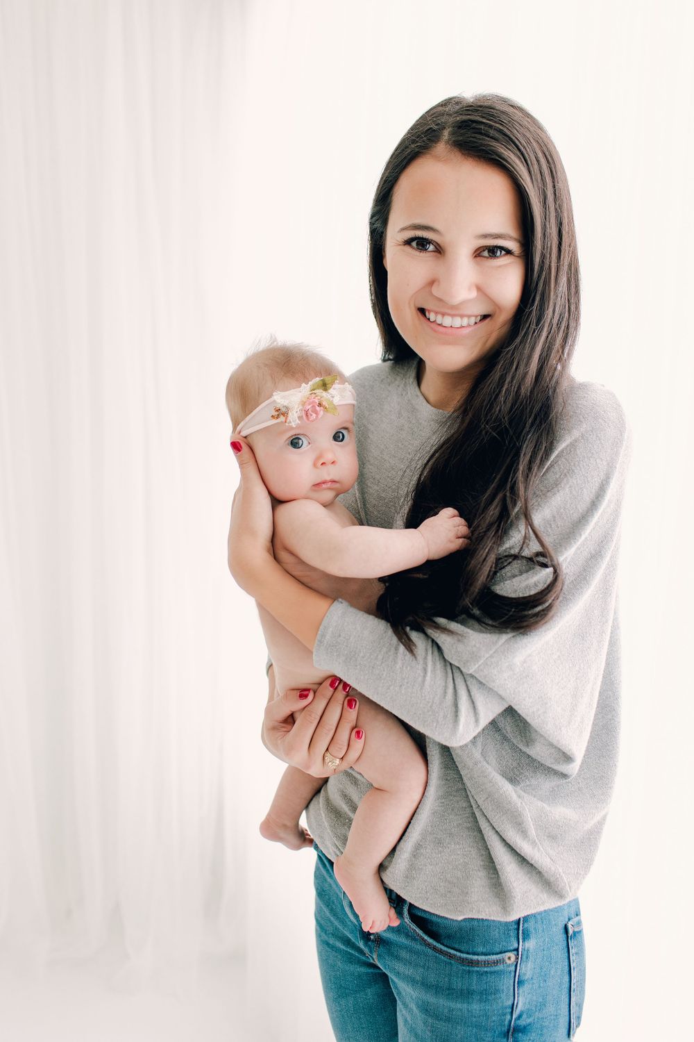 Portrait against white background showing parent in casual attire holding infant.