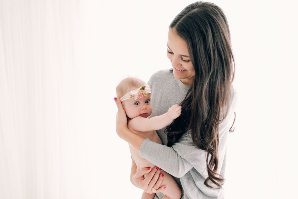 Parent wearing gray sweater holding infant against white background.