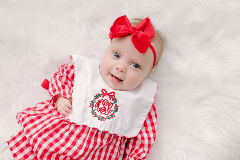 Smiling baby in red gingham dress with white bib and red bow headband.