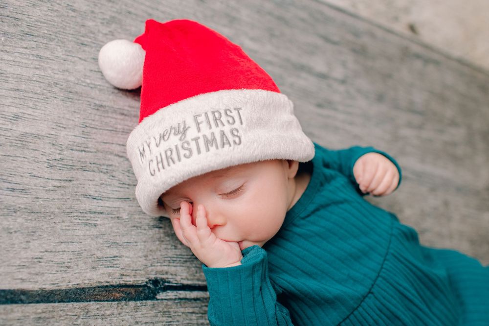 Sleeping baby wearing teal outfit and 'My First Christmas' Santa hat.
