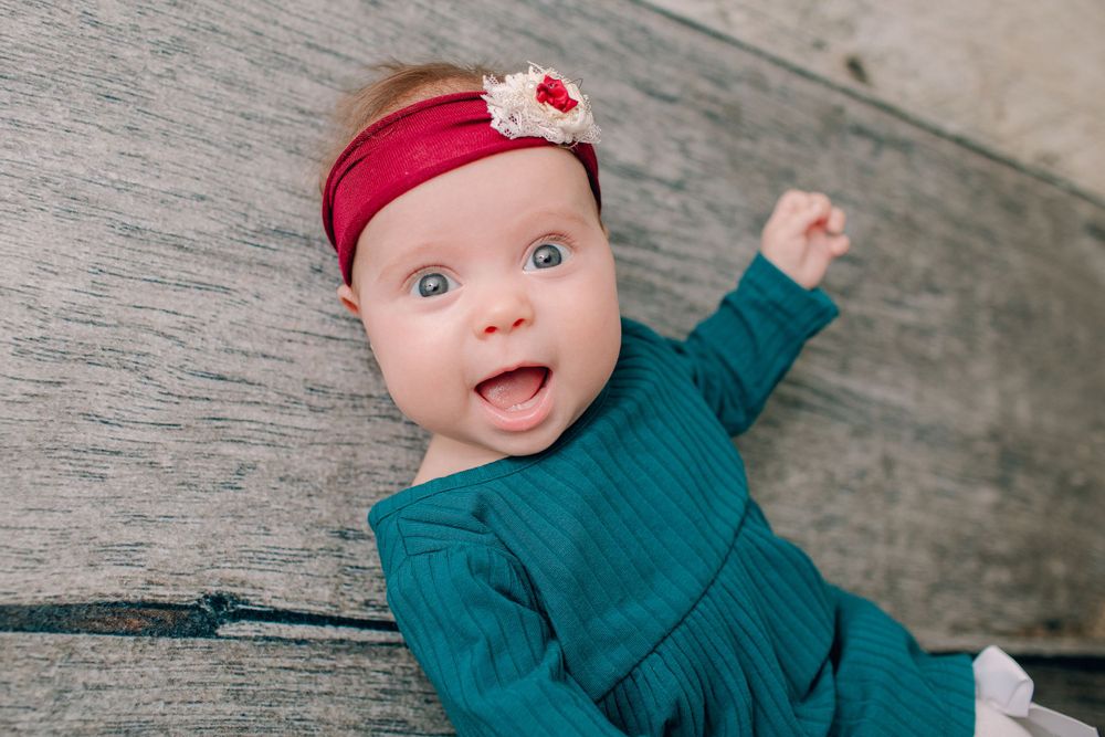 Excited baby in teal dress and red headband making expressive face.