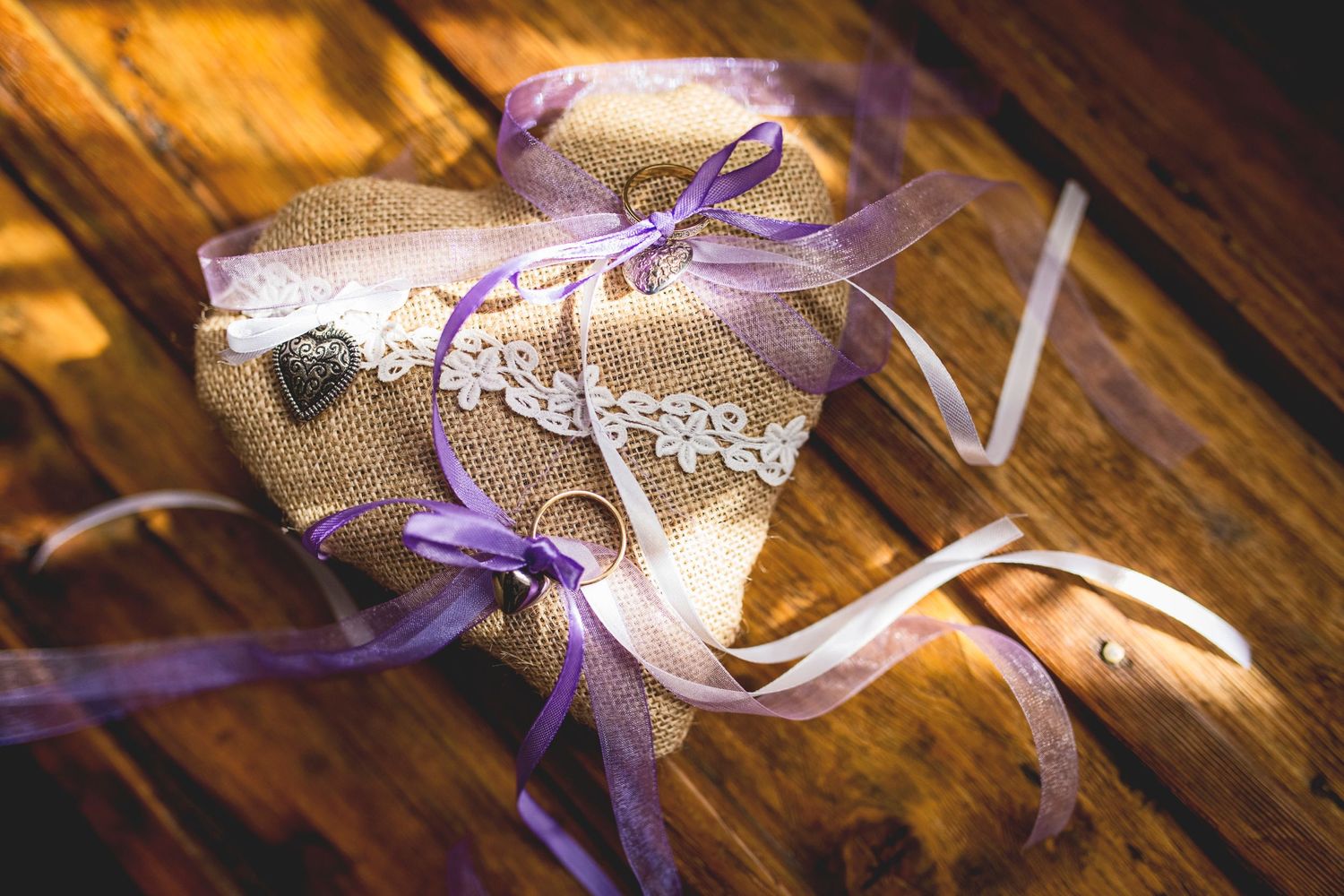 Wedding rings tied with purple ribbon on rustic lace and burlap decor.
