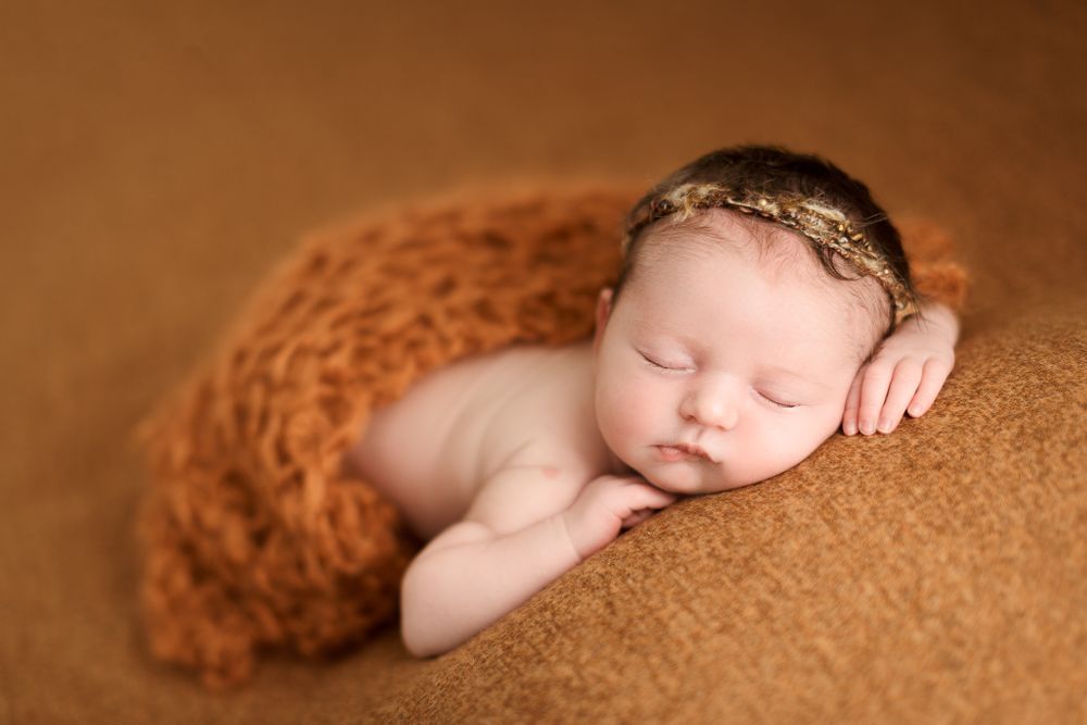 Posed newborn baby girl in studio on orange setup