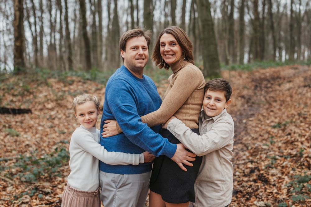 Family portrait in a wooded area with everyone wearing coordinating blue and tan outfits.