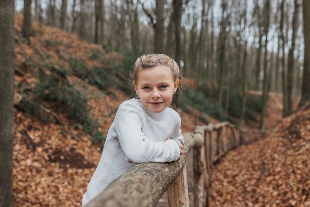 Person in white sweater leans against wooden railing on forest boardwalk during fall.