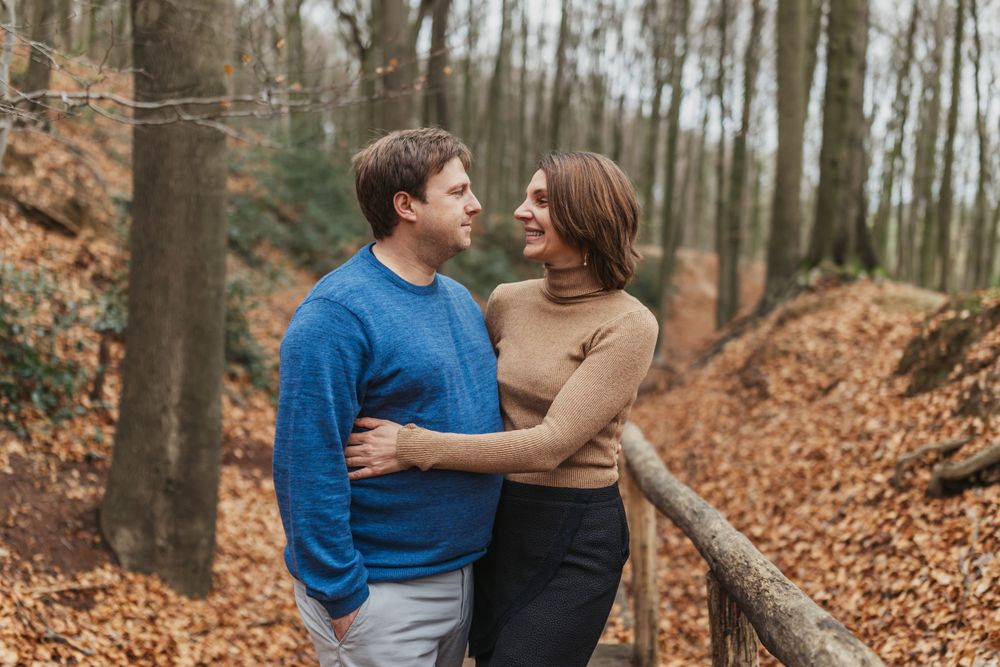 A couple shares an intimate moment on a wooden boardwalk surrounded by autumn leaves.