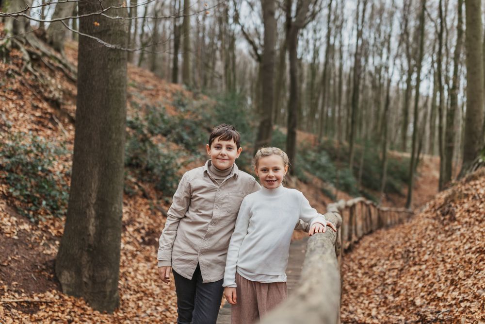 Two people stand together on a wooden boardwalk path through an autumn forest.