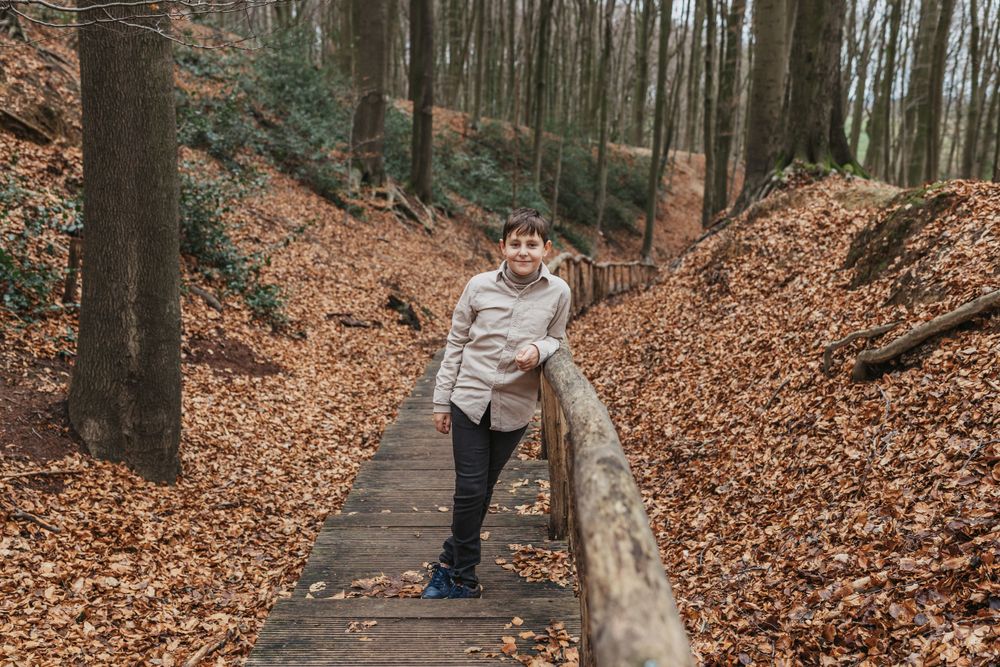 Person poses on a wooden walkway surrounded by fallen autumn leaves in the forest.