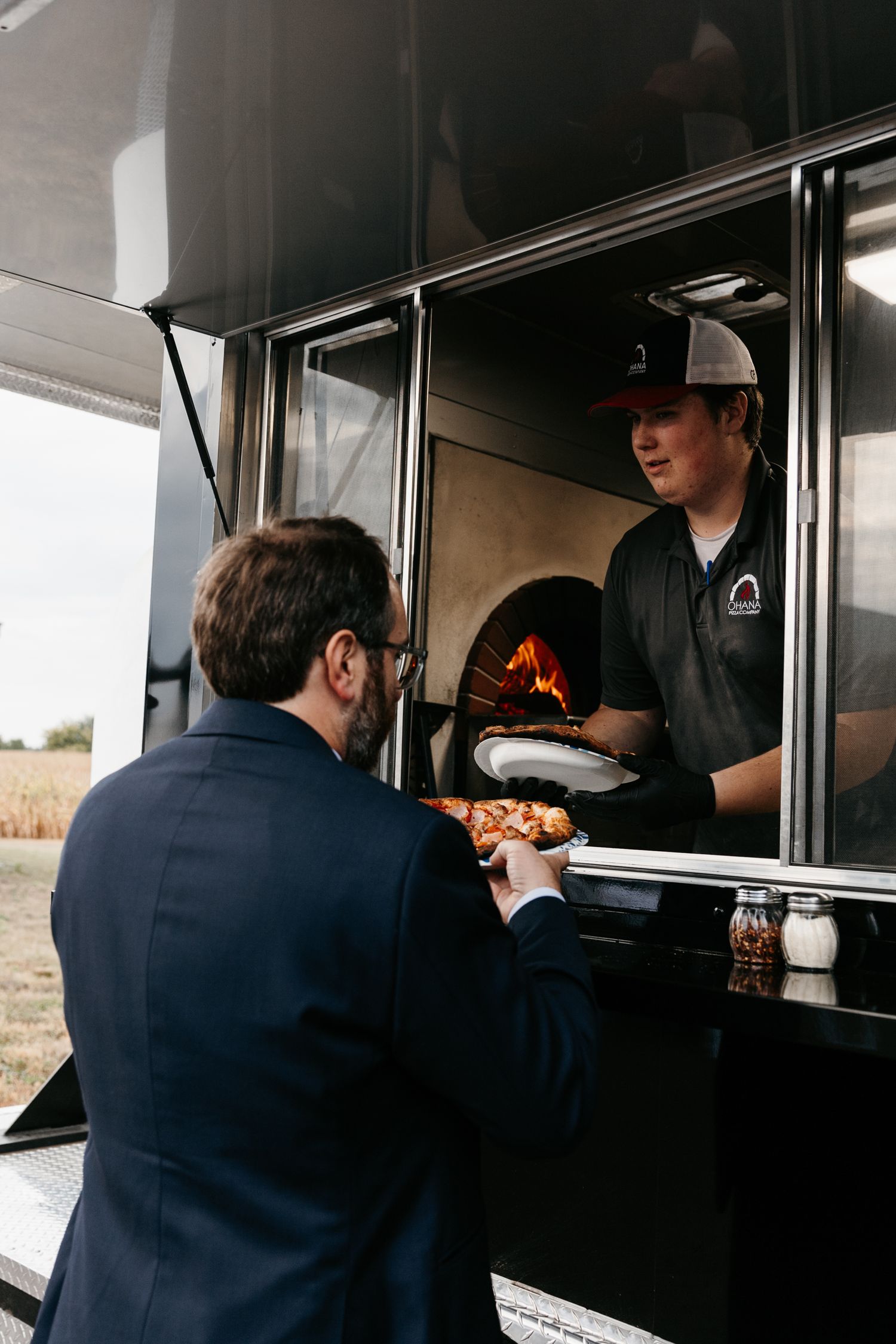 A customer ordering from a food truck with a wood-fired pizza oven visible inside.