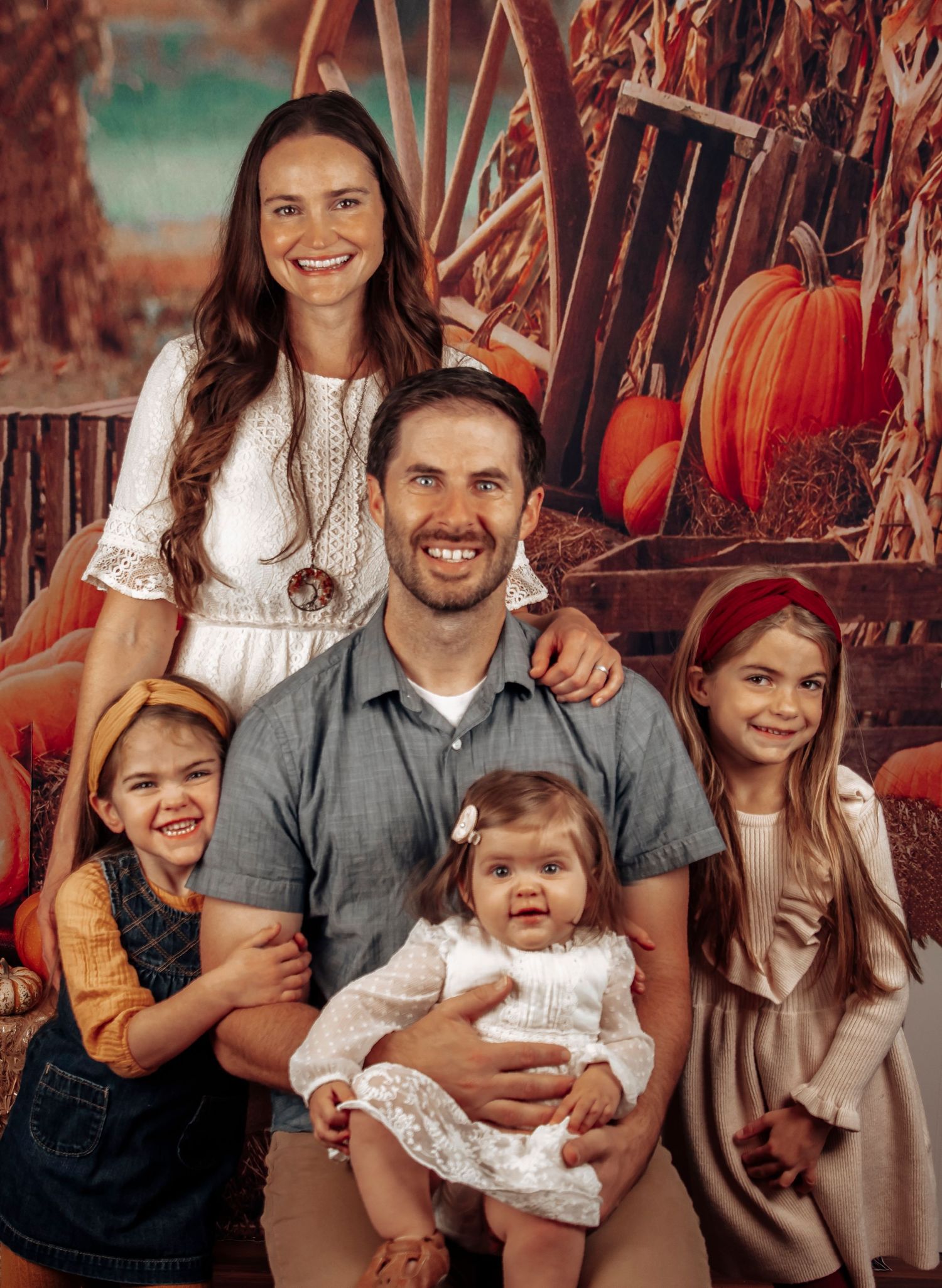 A happy family poses together for a fall portrait with pumpkins in the background.