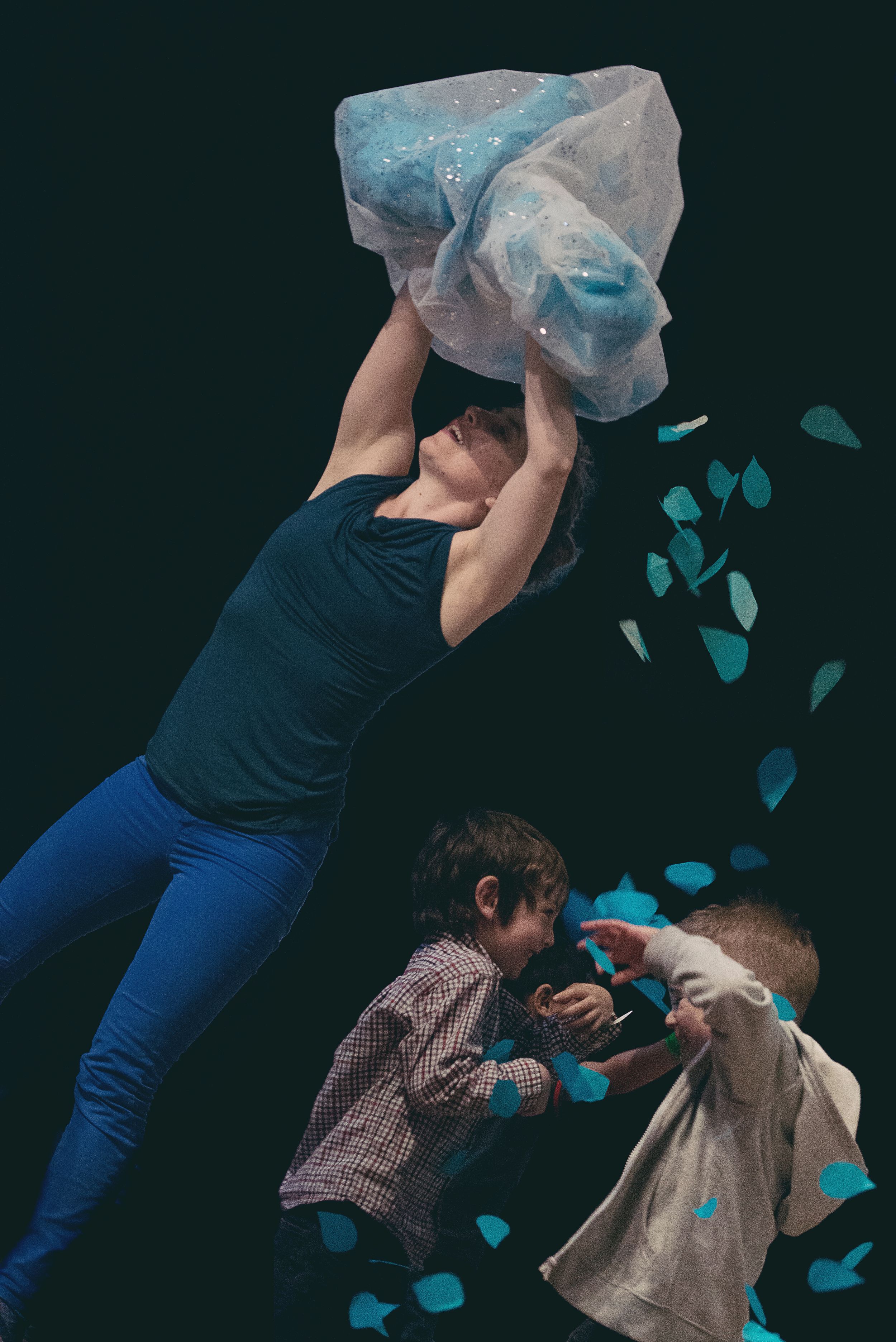 A Vancouver dance performance, Paper Playground, with people interacting with blue paper elements against a dark background. Photo by Riz H.
