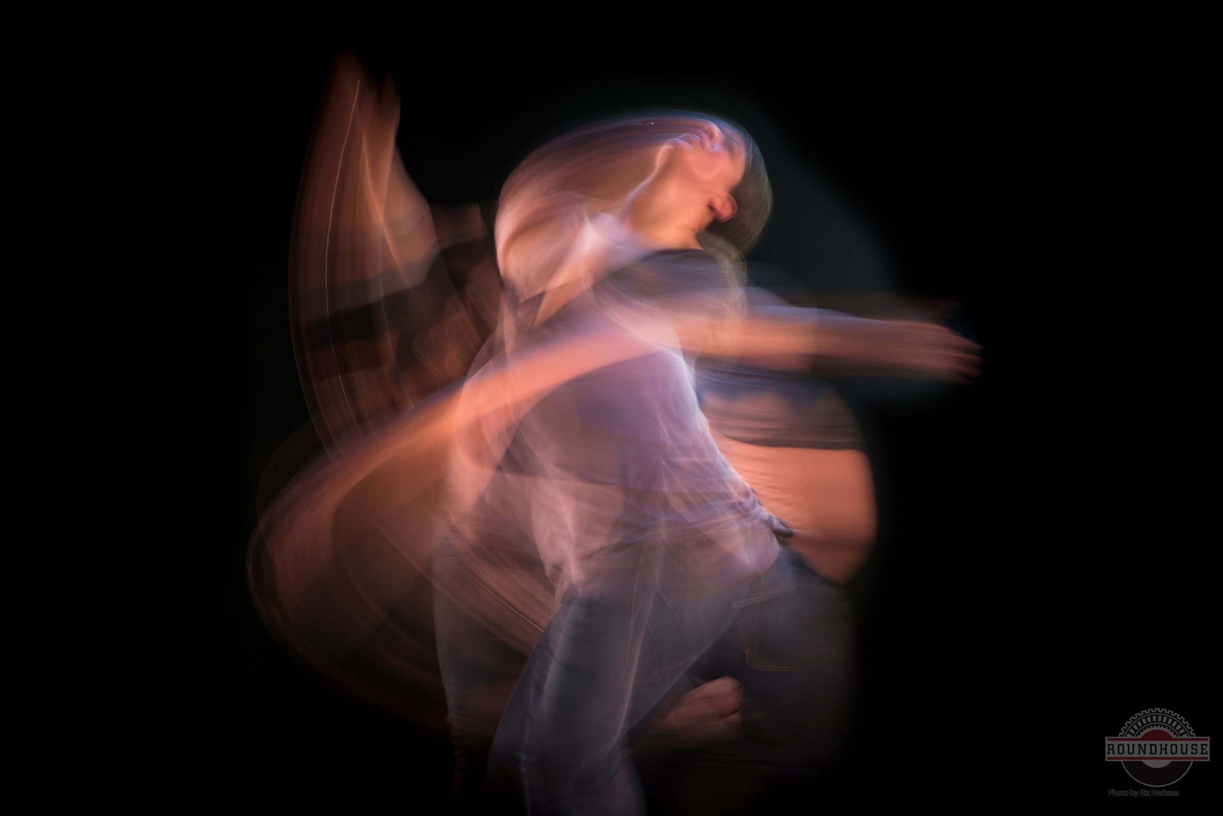 Long exposure photograph creates ethereal motion trails of a dancer in pink and orange hues. Photography by Riz Herbosa