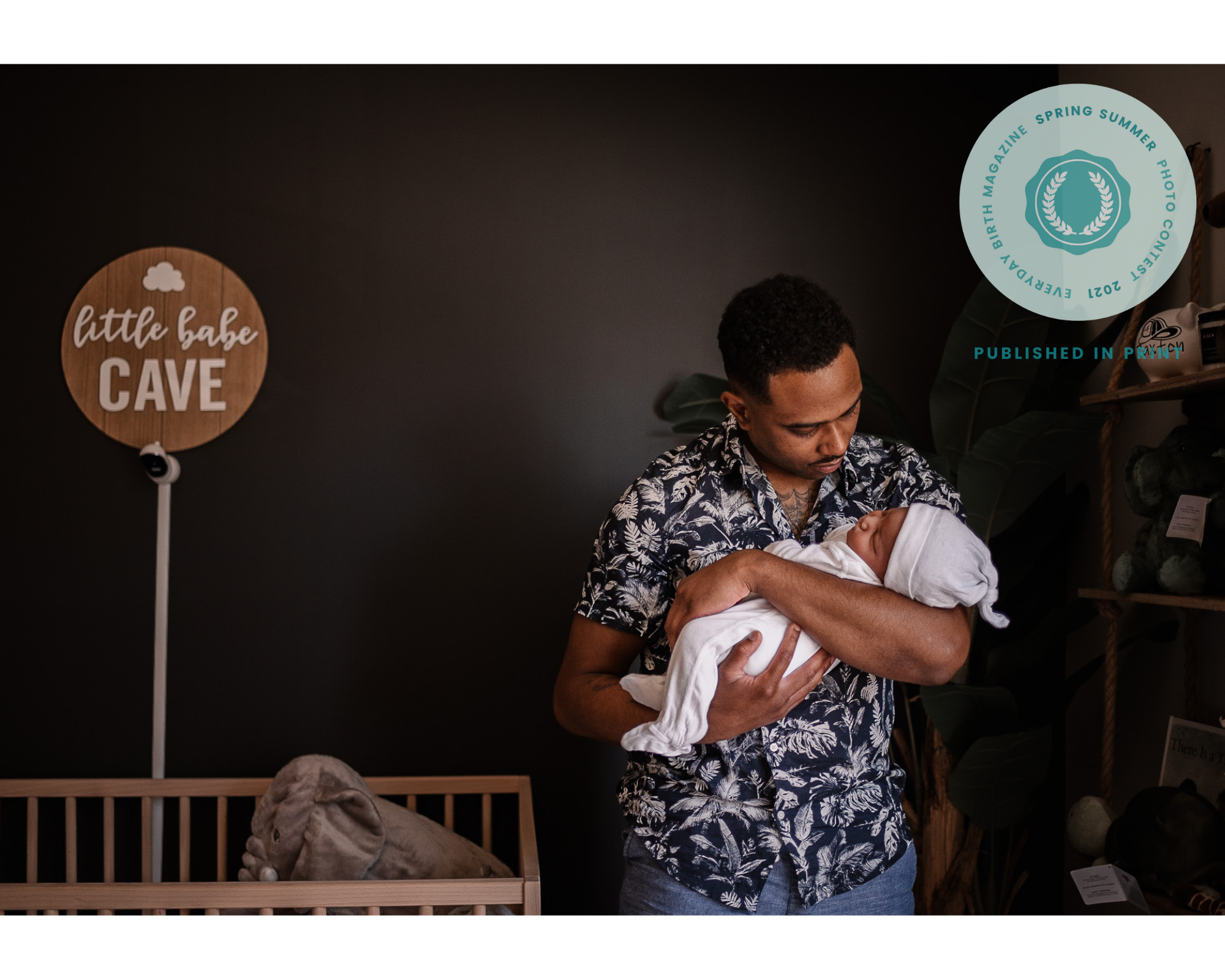 Black father holding a newborn wearing a hat while standing in baby nursery next to a crib
