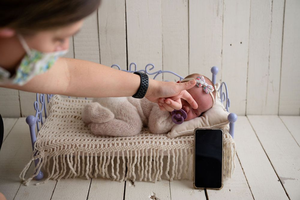 Baby laying on textured blanket while hand adjusts positioning against white wooden background.
