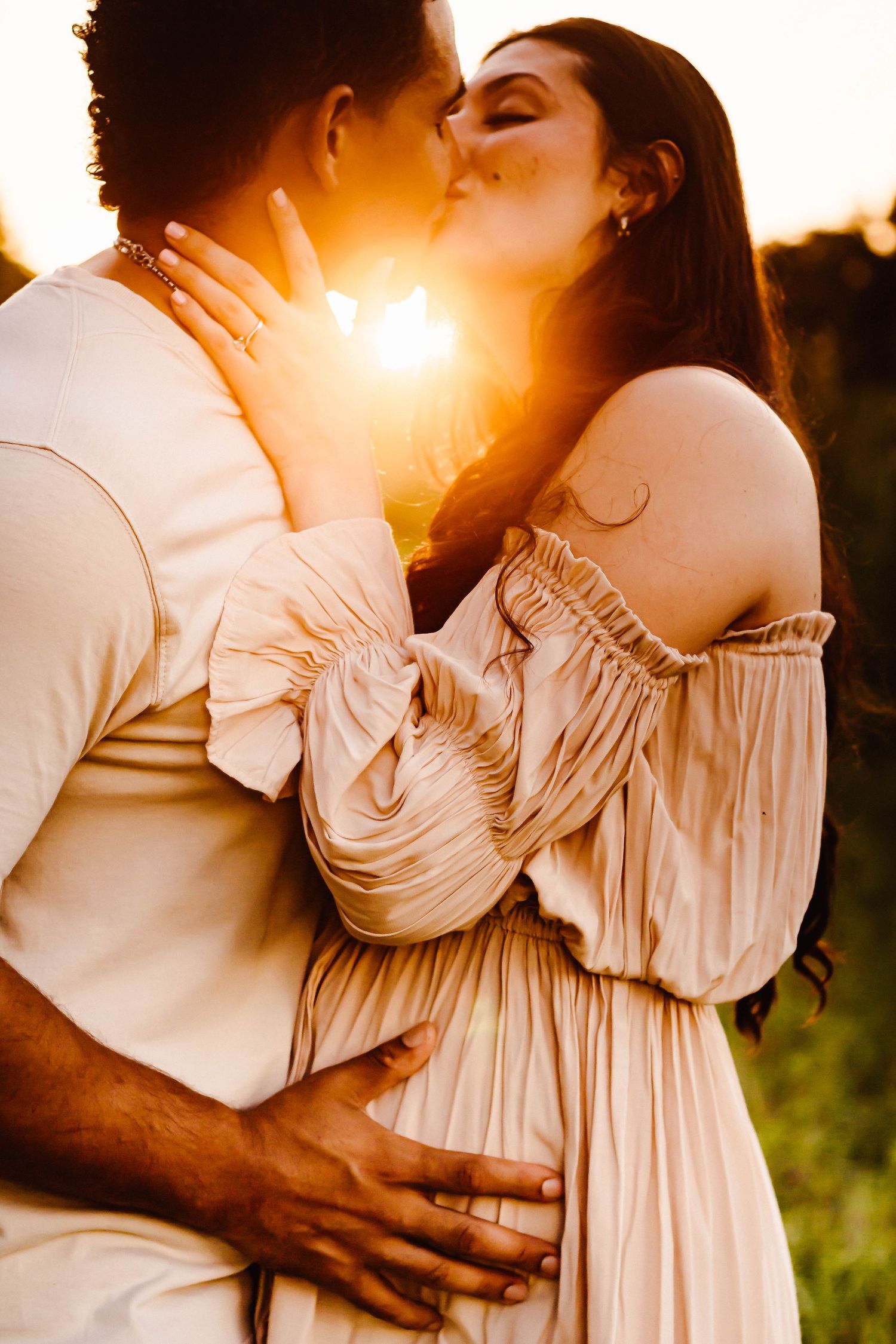 Couple embraces tenderly in flowing cream-colored clothing at sunset.