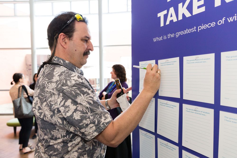 Someone writing on a blue wall display titled Take at an event. Mika Larson Photography.