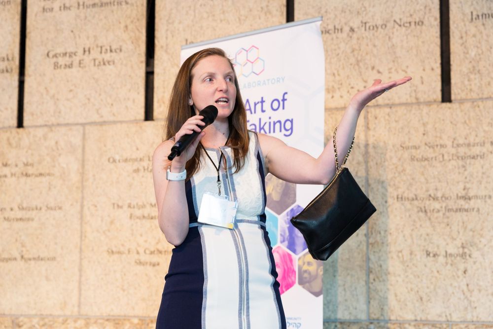 A speaker presents at a podium with 'The Art of Risk-Taking' banner visible in the background. Mika Larson Photography.