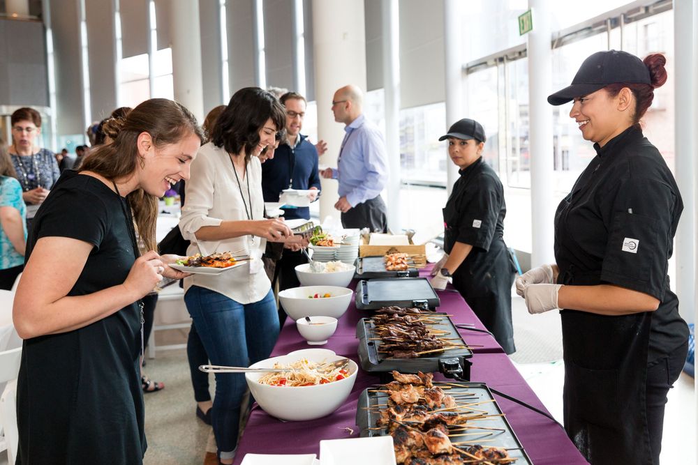 Event attendees select food from a catered buffet line with purple tablecloth. Mika Larson Photography.