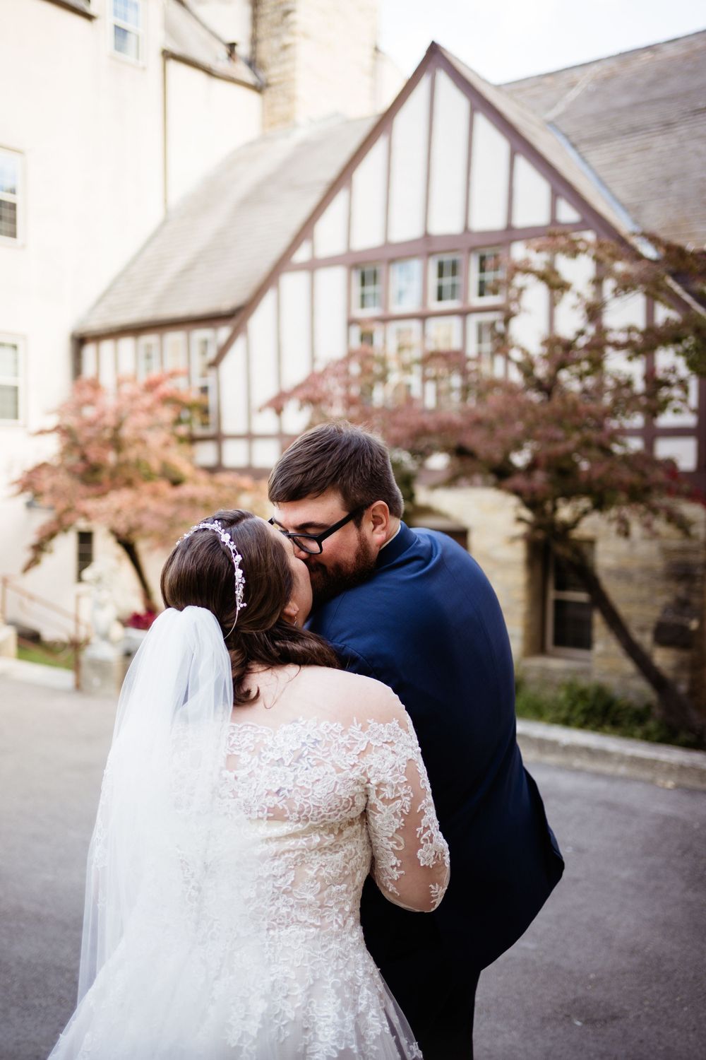 A tender wedding moment captured outside a Tudor-style building with autumn foliage.