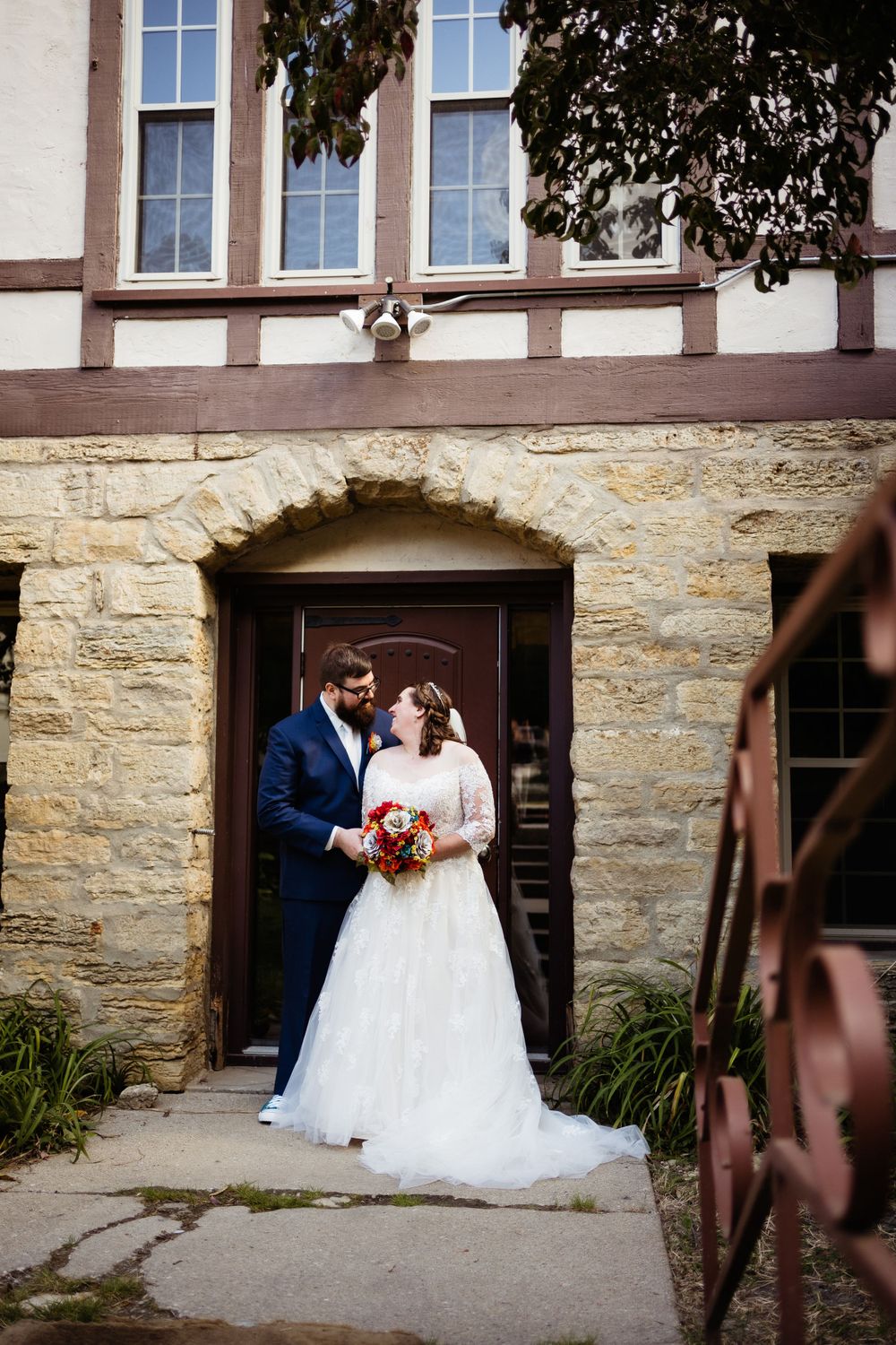 A wedding couple poses in a stone archway entrance of a historic building.