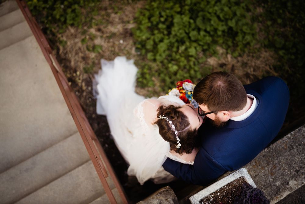 A couple sits on stone steps during their wedding day, viewed from above.