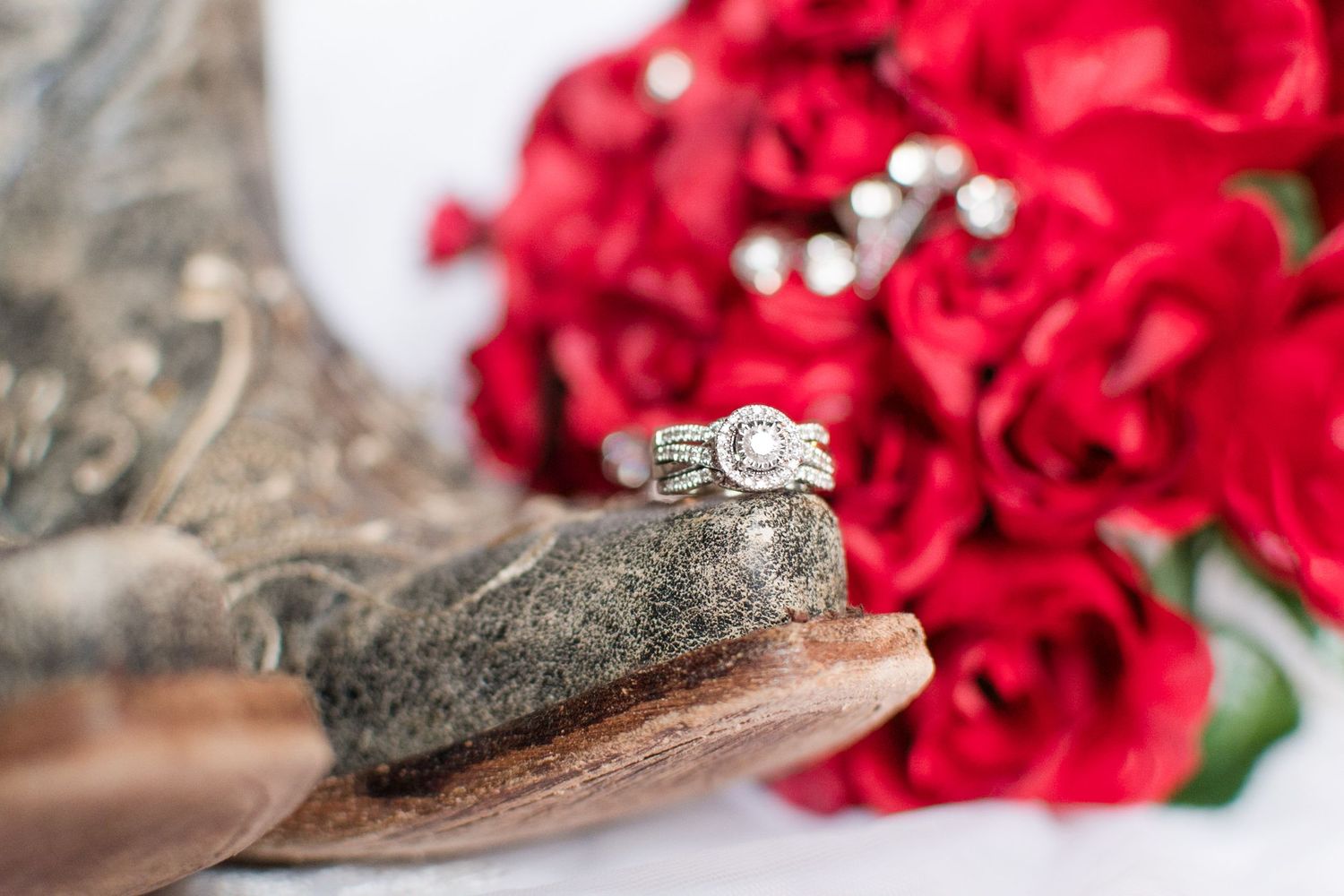 Wedding rings displayed on rustic wood with red roses in background.