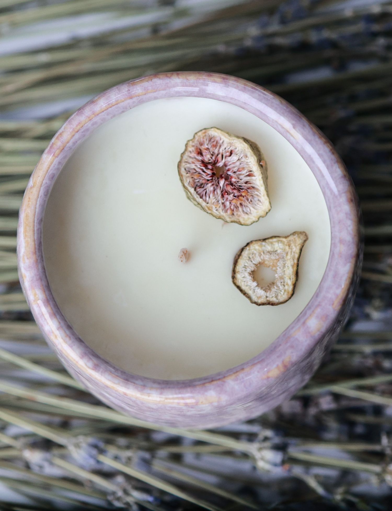 White candle decorated with dried fig slices in a pink ceramic container.