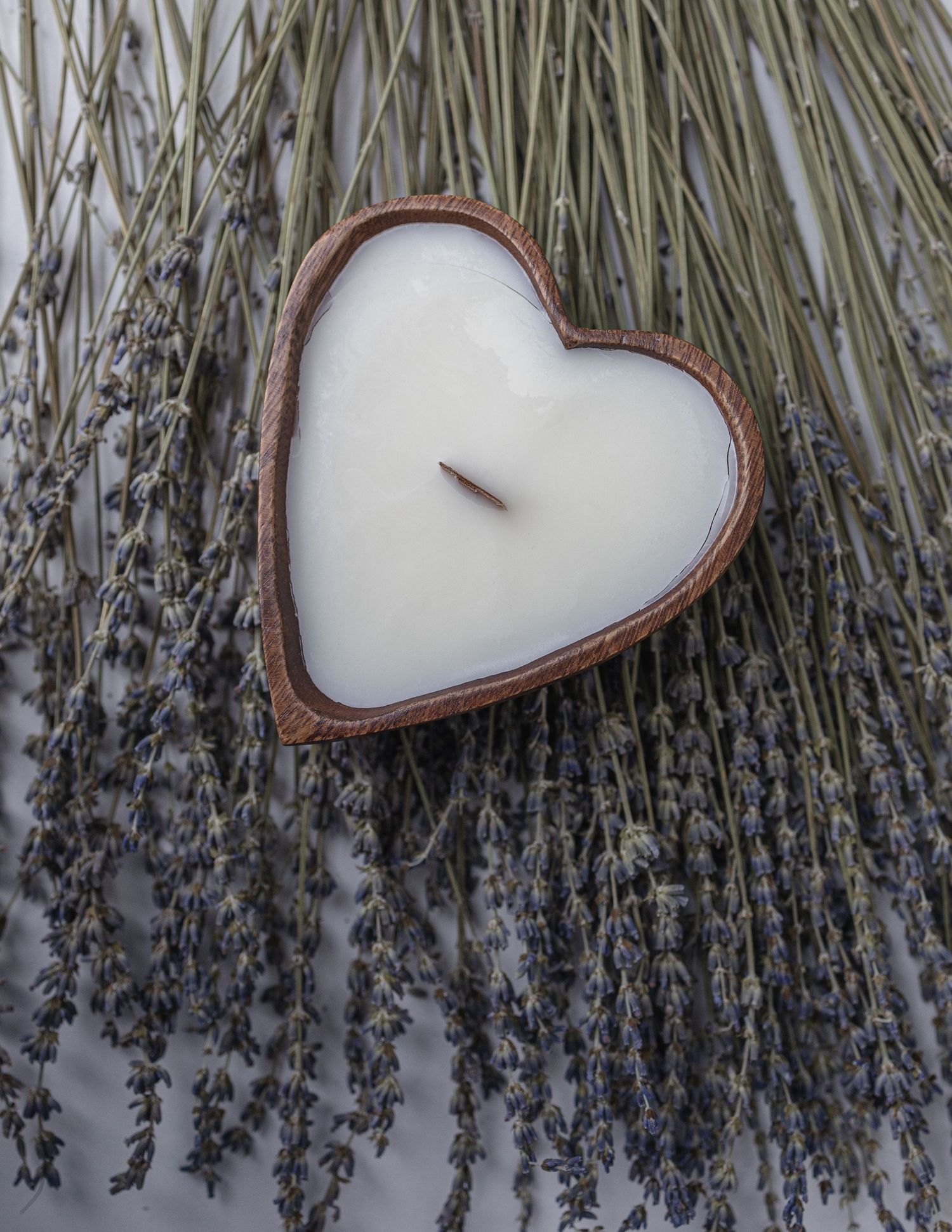 Heart-shaped white candle nestled among dried lavender stems.