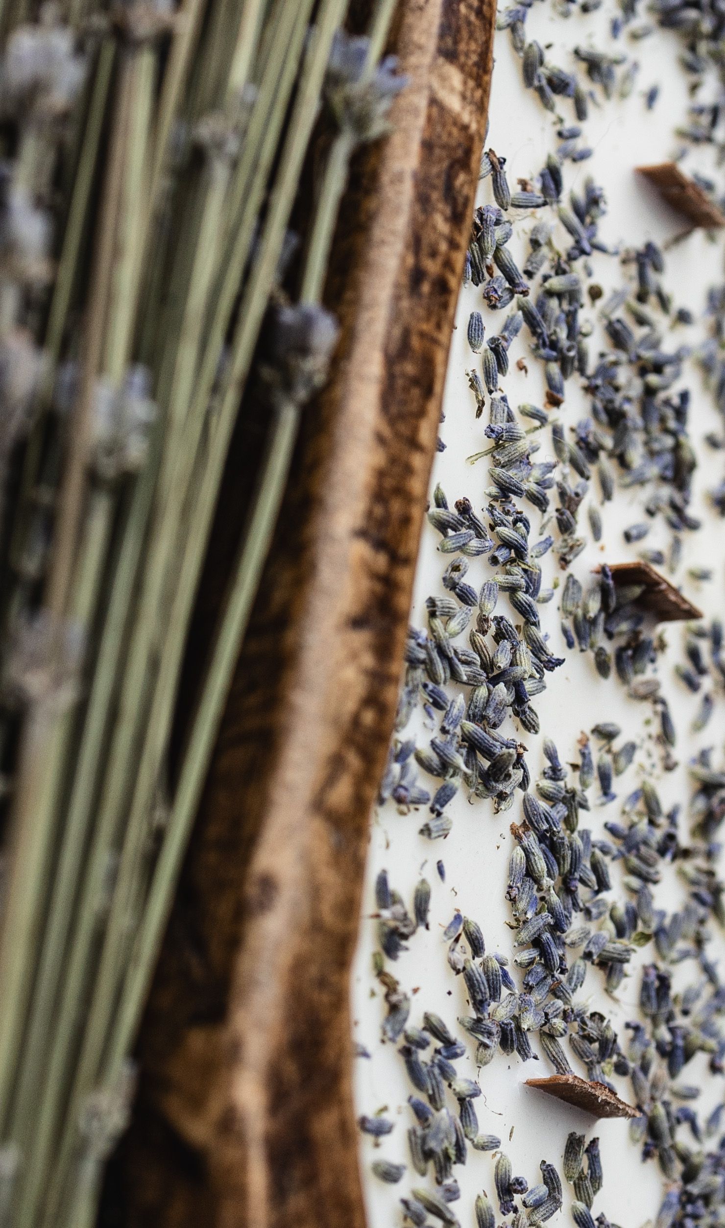 Dried lavender buds scattered on a white surface with wooden elements in the background.
