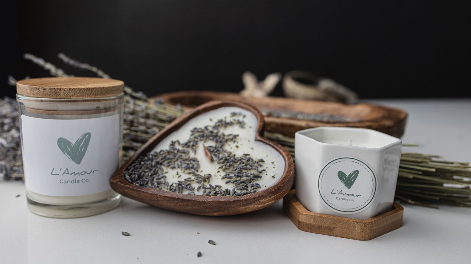 Wood-lidded candles with heart logos arranged with dried lavender and wooden heart dishes.
