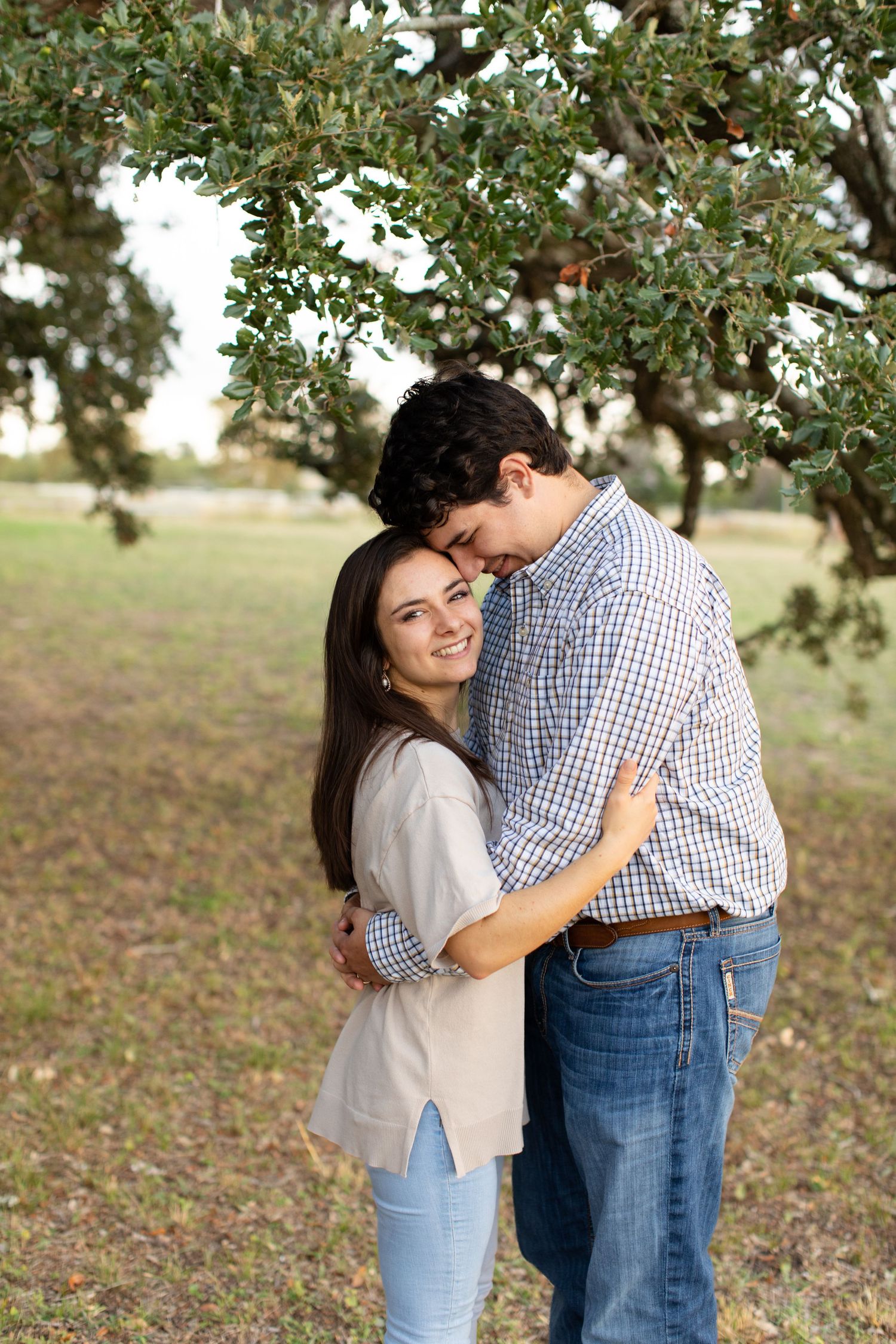 A romantic moment captured beneath leafy green trees in natural lighting.