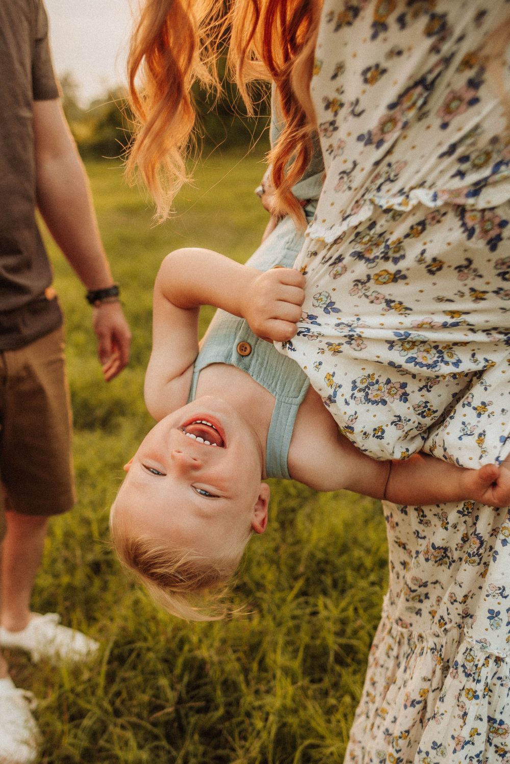 Playful moment captured in a field with floral dress and joyful expressions.