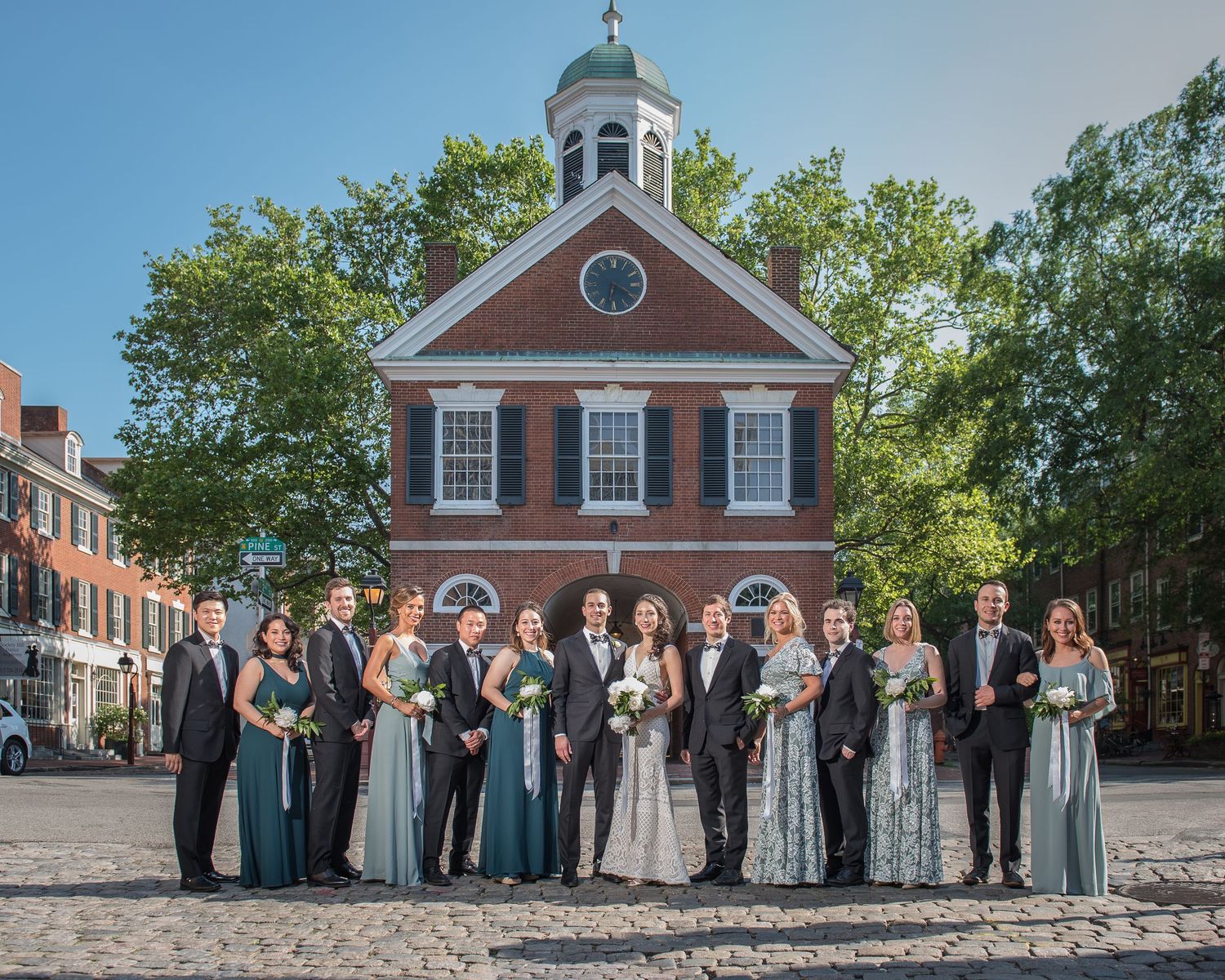 A formal wedding party lined up in front of a classic colonial brick building.