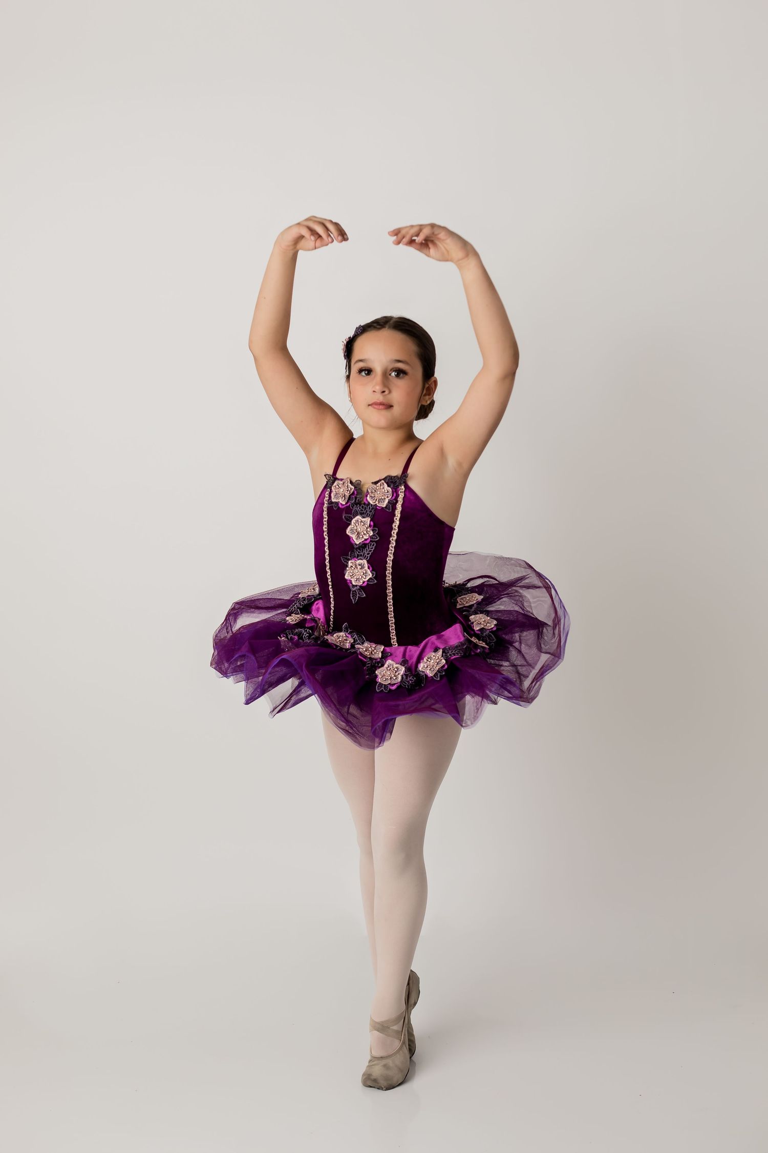 Ballerina dressed in a purple tutu posing for her dance portrait session with a solid white background at the studio.