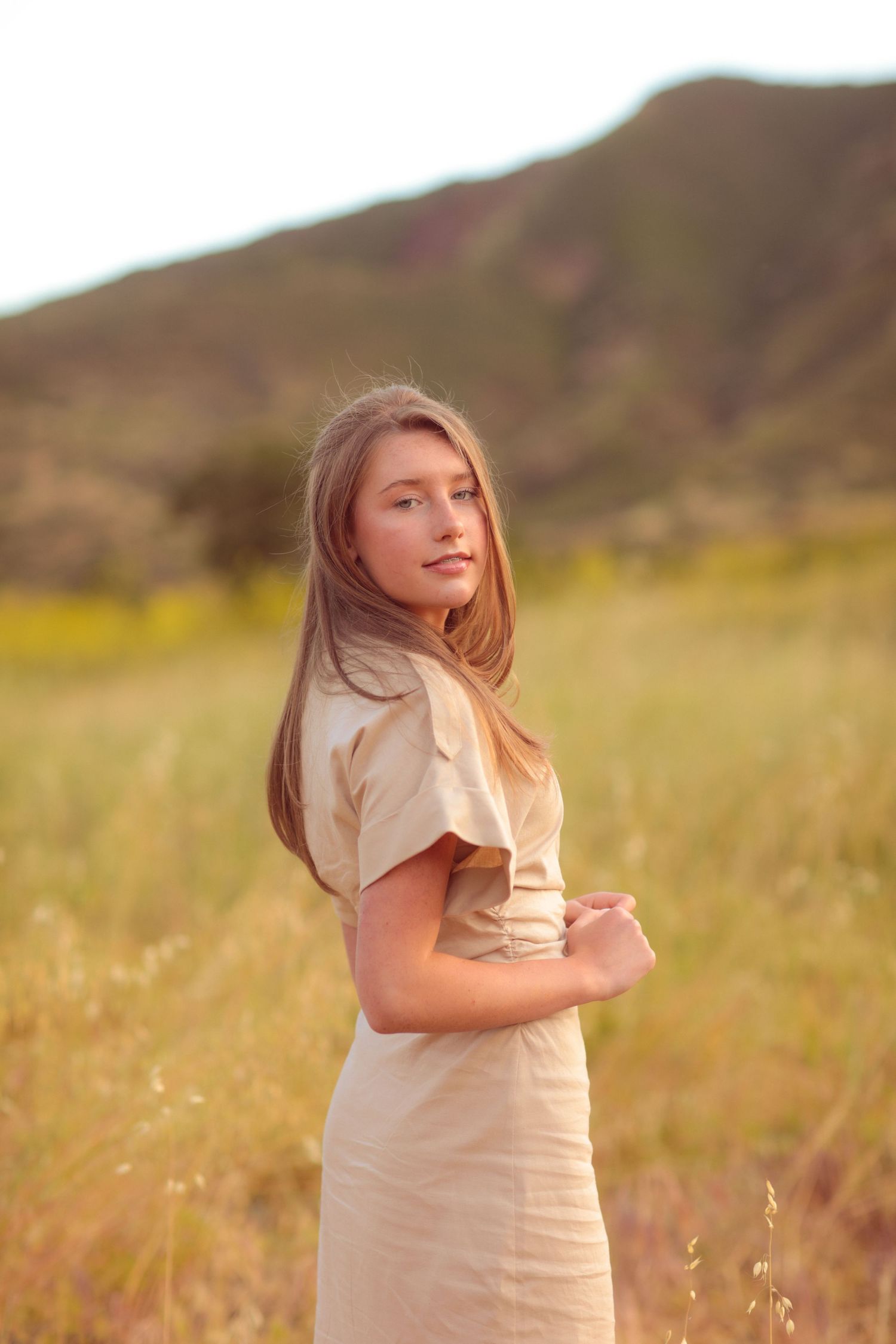 A dreamy portrait of a young person in a cream dress against a mountain backdrop.