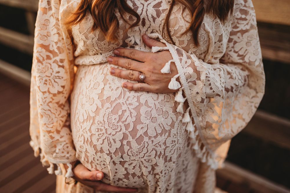 Close-up of hands cradling a pregnant belly in a white lace dress.