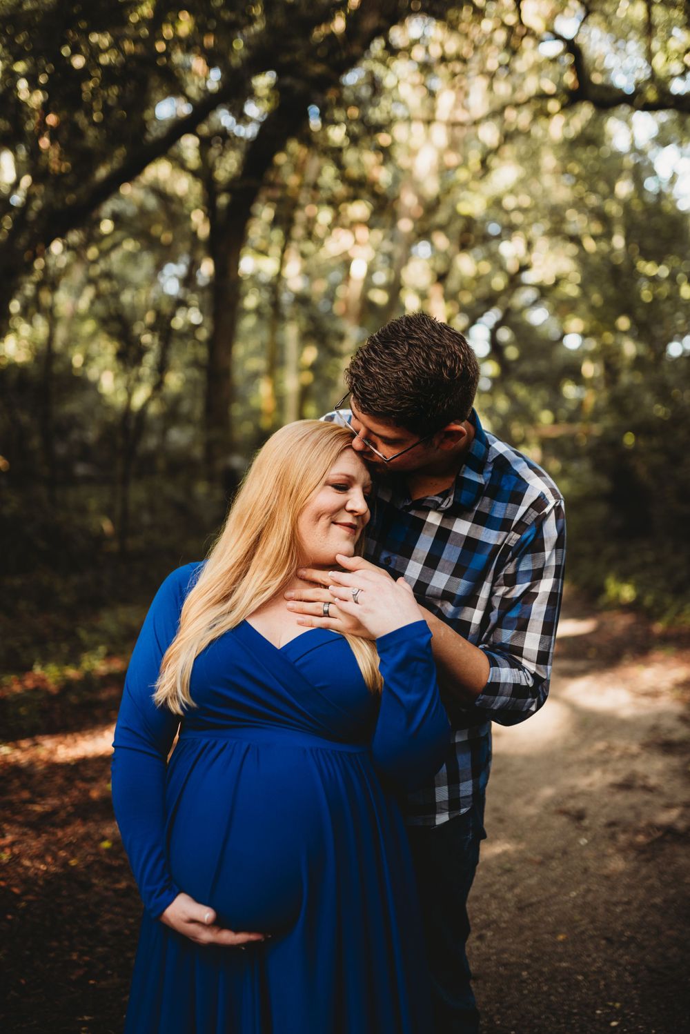 Intimate maternity moment captured in the woods with couple wearing blue dress and plaid shirt.