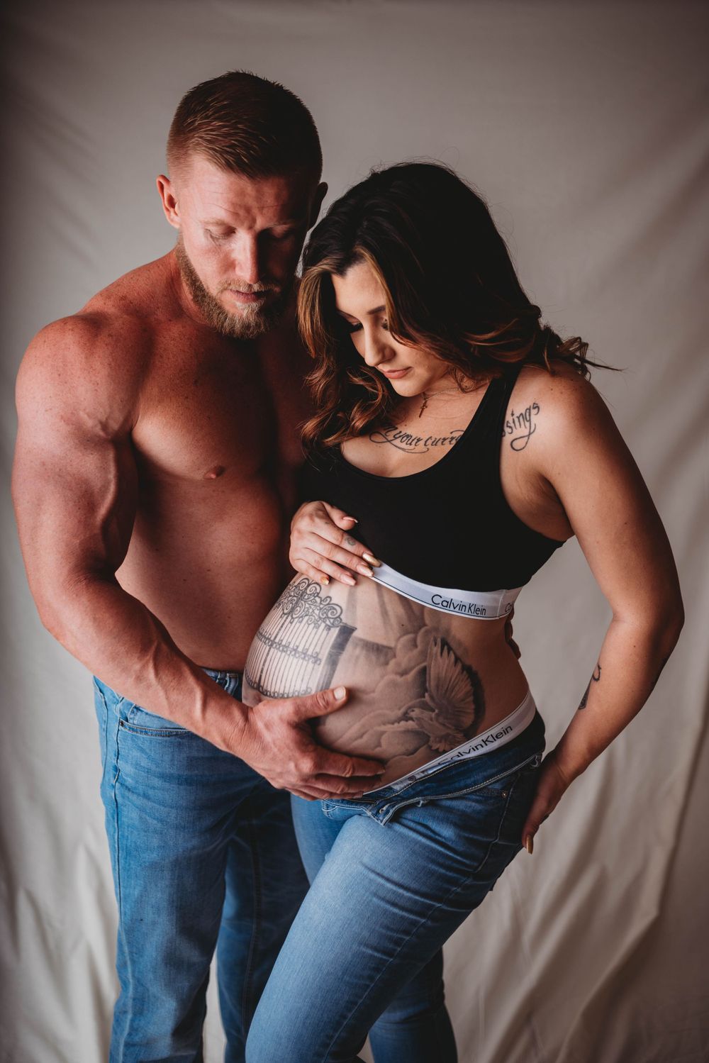 Intimate studio maternity photo featuring a couple with belly art in casual attire.